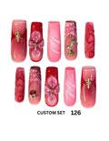 Ten pink and red press-on nails with decorative floral, swirl, and metallic embellishments. 