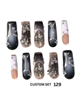 The nails feature marbled black, gray, and beige designs, silver rhinestone embellishments, and nude pink tips.