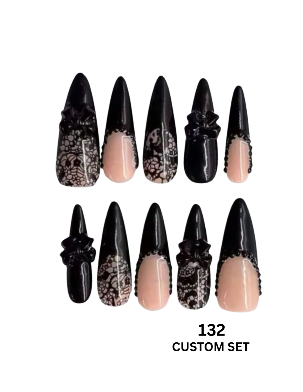 A set of 10 custom stiletto press-on nails  feature a glossy black top half with intricate black-and-white lace patterns and 3D black floral embellishments, paired with a sheer nude-pink bottom half.