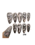 Press-on nails with one nail shown applied to a finger. The nails have a glossy silver metallic finish with a raised abstract organic pattern over a pale white base.