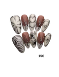 Almond-shaped press-on nails with various designs including white with black leaf and swirl patterns, white with black stars, and a dusty rose pink with black leaf and heart designs. 
