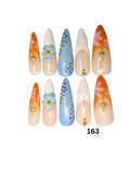 Set of 10 false press-on nails, featuring orange gradient designs with pink floral patterns, light blue gradient designs with gold star details, and white gradient designs with small gold dots.